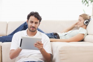 Man using a tablet computer while his girlfriend is listening to music